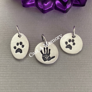 three tiny silver charms showing a paw print and hand print